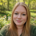 Close-up portrait of a woman with long blonde hair, smiling in a sunlit garden.