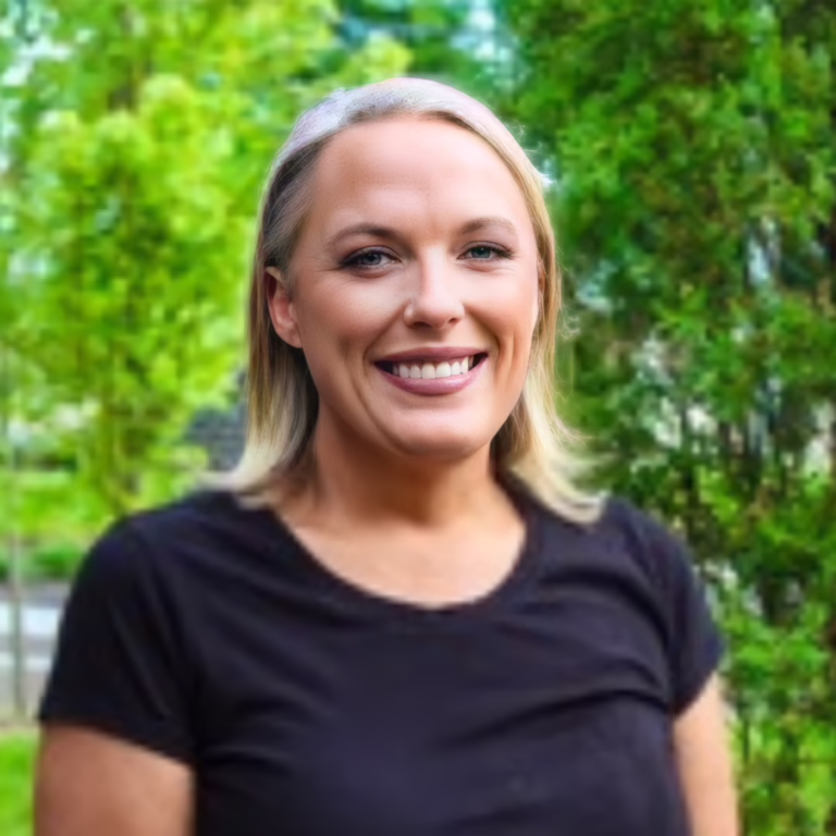 Smiling woman with blonde hair wearing a black shirt, outdoors in a green park.