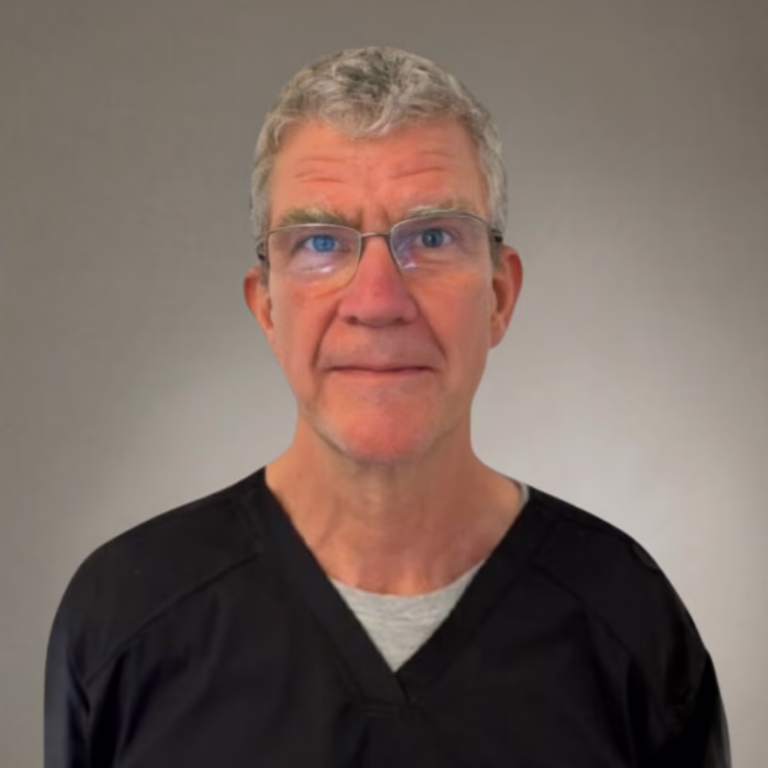Portrait of a middle-aged man with gray hair and glasses, wearing black scrubs, against a neutral gray background.
