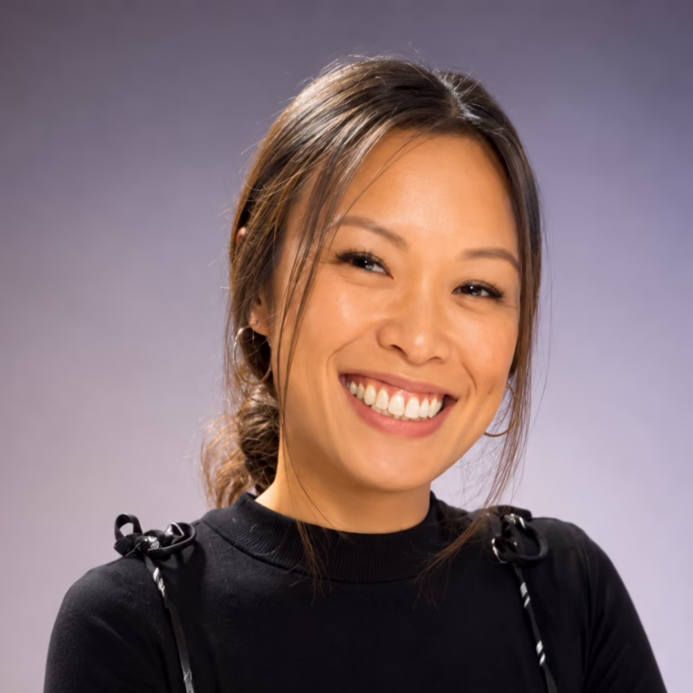 Smiling Asian woman with dark hair in a black top, against a neutral gray background.