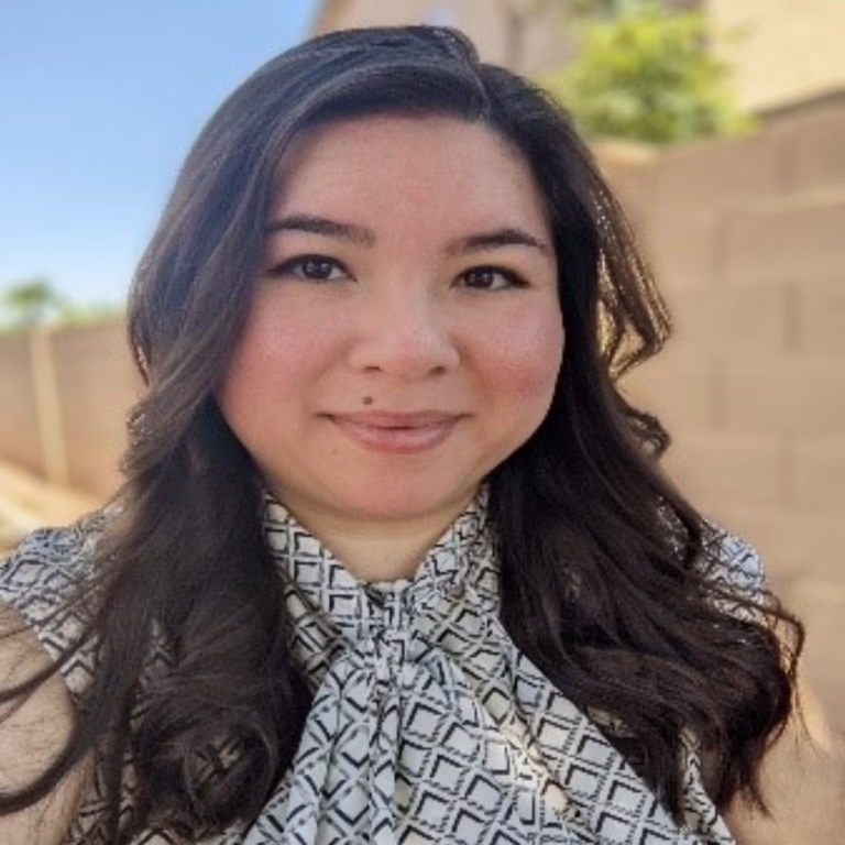 Portrait of a smiling woman outdoors, with long dark hair and a patterned blouse.