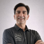 Professional head-and-shoulders portrait of a smiling man in a dark polo shirt with a logo that reads 'Smiles on Clark' and 'Dr. E. Waked' on the chest.