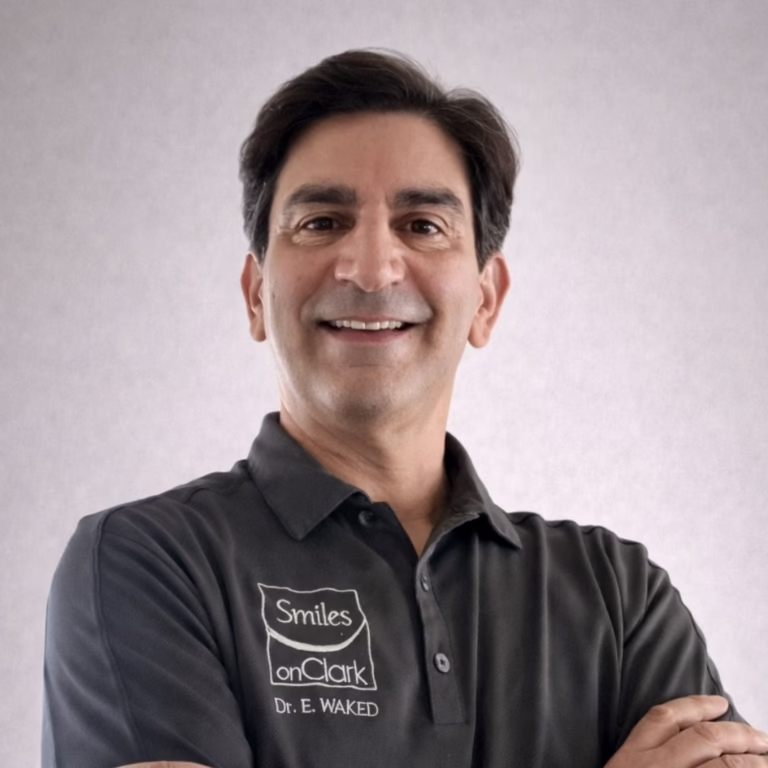 Professional head-and-shoulders portrait of a smiling man in a dark polo shirt with a logo that reads 'Smiles on Clark' and 'Dr. E. Waked' on the chest.